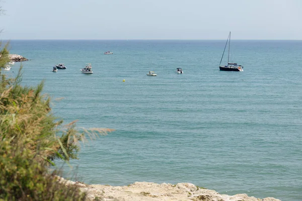 Selective focus of boats and yacht in sea and green plants on coast in Catalonia, Spain — Stock Photo