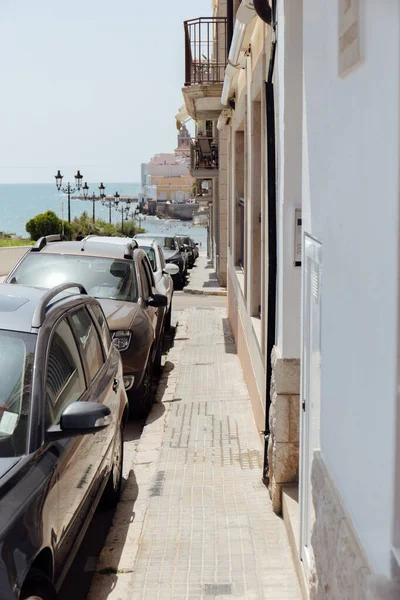 Strada urbana con fila di auto, edifici e mare con cielo blu sullo sfondo in Catalogna, Spagna — Foto stock