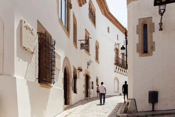 CATALONIA, SPAIN - APRIL 30, 2020: People walking on sunlight street near buildings with white facades — Stock Photo