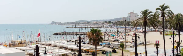 Каталония, Испания - 30 апреля 2020 года: Панорамный снимок городской улицы с яхтами на берегу моря и гор с голубым небом на заднем плане — стоковое фото