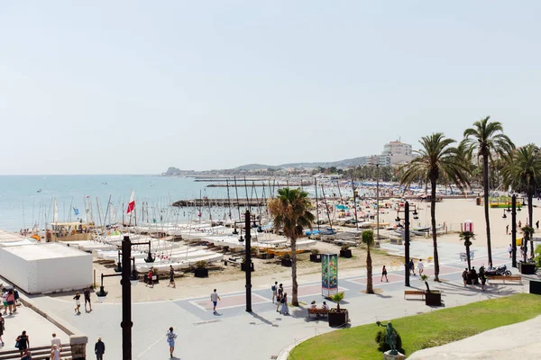 CATALONIA, SPAIN - APRIL 30, 2020: People walking on urban street near yachts, palm trees and clear sky at background — Stock Photo