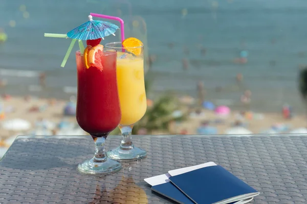 Glasses of cocktails and passports with air tickets on table with beach at background — Stock Photo