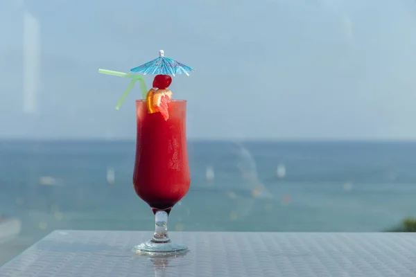 Bicchiere di cocktail con ombrellone e cannucce da bere sul tavolo con mare e cielo azzurro sullo sfondo — Foto stock