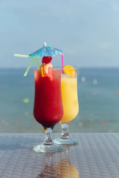 Two glasses of cocktails with drinking straws on table and sea with sky at background — Stock Photo