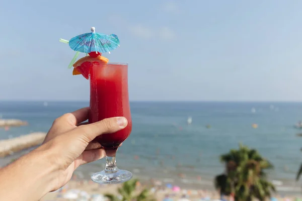 Cropped view of man holding glass of cocktail with seascape and blue sky at background — Stock Photo