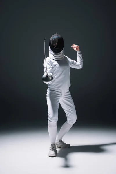Fencer in fencing mask and suit training under spotlight on black background — Stock Photo
