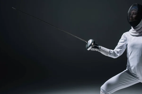 Cropped view of fencer in fencing mask holding rapier on black background — Stock Photo