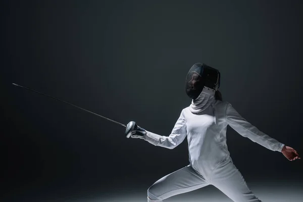 Fencer in fencing mask exercising on black background — Stock Photo