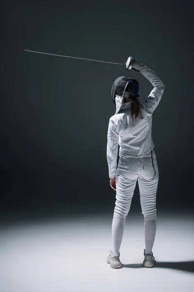 Back view of fencer in fencing mask holding rapier on black background — Stock Photo