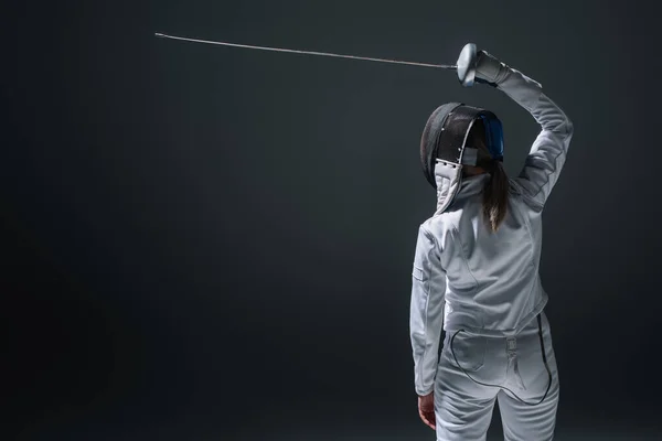 Back view of fencer holding rapier above head isolated on black — Stock Photo