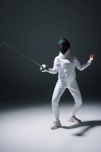 Fencer in fencing mask training with rapier on white surface on black background — Stock Photo