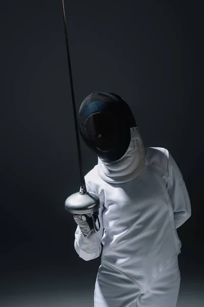 Fencer in fencing mask holding rapier isolated on black — Stock Photo