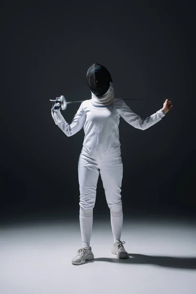 Fechterin mit Fechtmaske hält Degen im Scheinwerferlicht auf schwarzem Hintergrund — Stockfoto