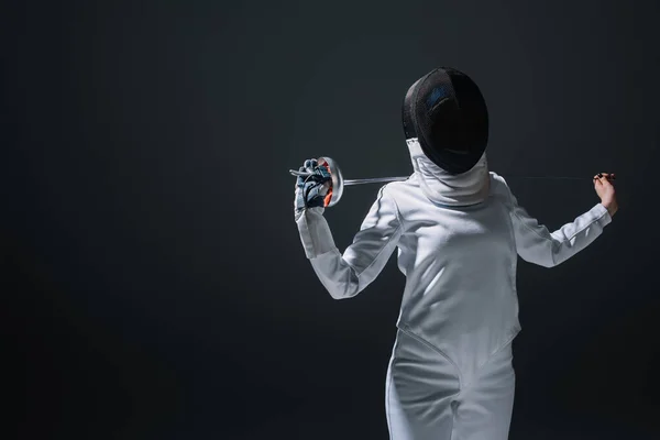 Fencer in fencing suit, mask and glove holding rapier isolated on black — Stock Photo