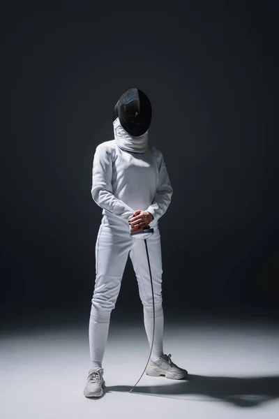 Fencer in fencing mask holding rapier under spotlight on black background — Stock Photo