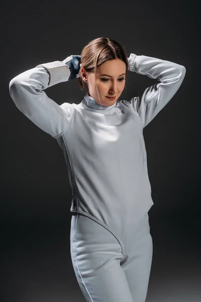 Fencer in fencing suit plaiting hair isolated on black — Stock Photo