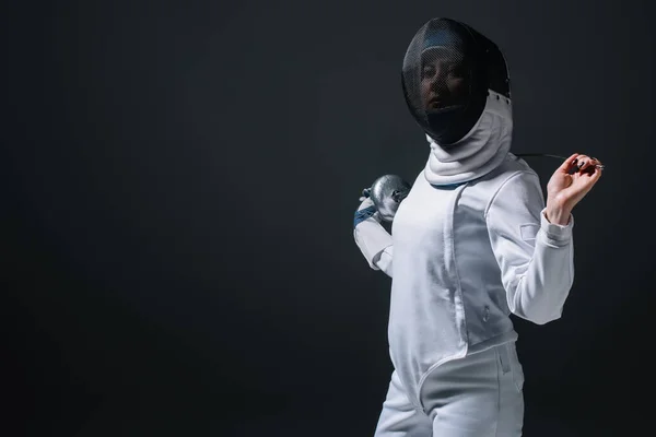 Fencer in fencing mask looking at camera while holding rapier isolated on black — Stock Photo