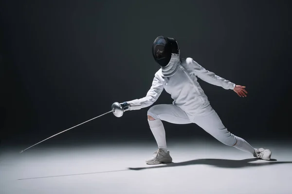 Fencer training under spotlight on black background — Stock Photo