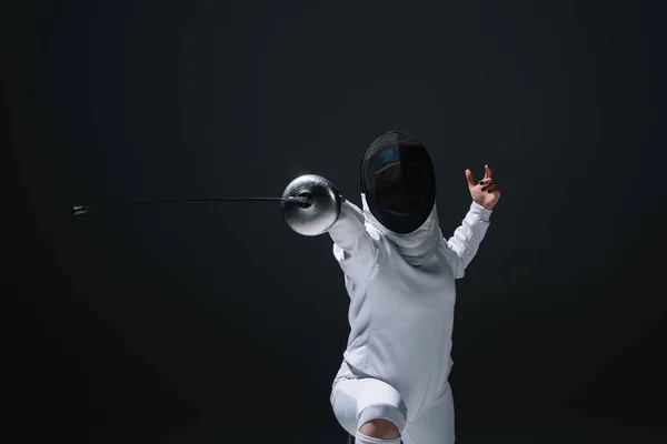 Fencer in fencing mask exercising with rapier isolated on black — Stock Photo
