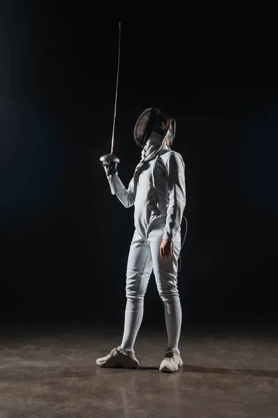 Fencer in fencing mask holding rapier on black background — Stock Photo