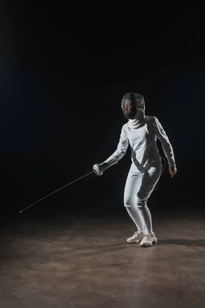 Escrimeuse en costume d'escrime et masque d'entraînement avec rapière sur fond noir — Photo de stock