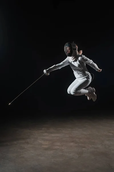 Fencer in fencing mask holding rapier and jumping on black background — Stock Photo