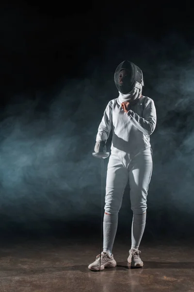 Fencer adjusting fencing mask on black background with smoke — Stock Photo