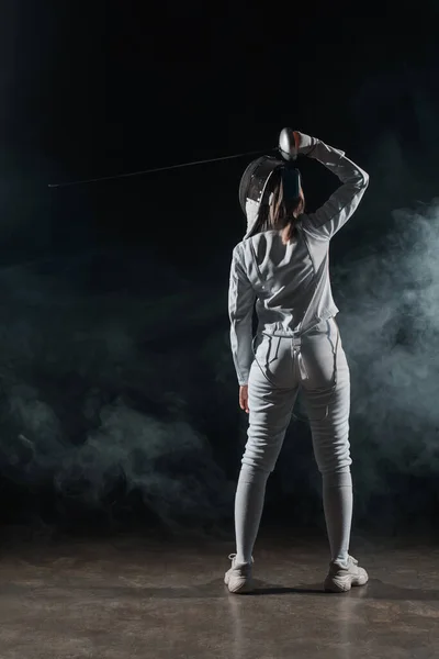 Back view of swordswoman fencing on black background with smoke — Stock Photo