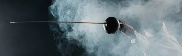 Foto panorámica de esgrima sujetando el estoque sobre fondo negro con humo - foto de stock