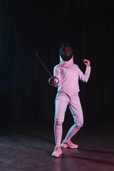 Fencer in fencing mask and suit holding rapier on black background — Stock Photo