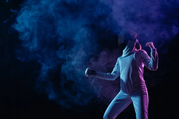 Fencer exercising with rapier on black background with smoke — Stock Photo