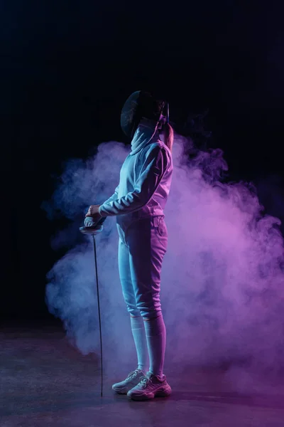 Side view of fencer holding rapier on black background with smoke — Stock Photo