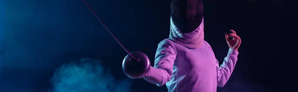 Panoramic crop of swordswoman fencing on black background with smoke and lighting — Stock Photo