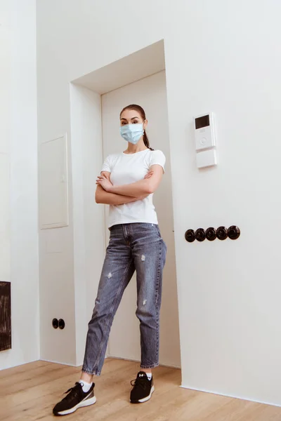 Mujer en máscara médica con brazos cruzados mirando a la cámara en el pasillo - foto de stock