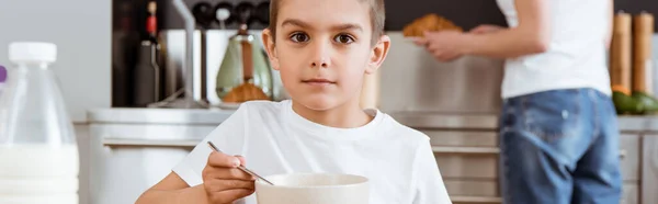 Panoramic crop of boy looking at camera while eating breakfast in kitchen — Stock Photo