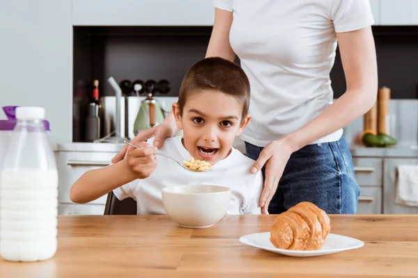 Selektiver Fokus des Jungen, der in der Küche neben der Mutter Getreide isst — Stockfoto