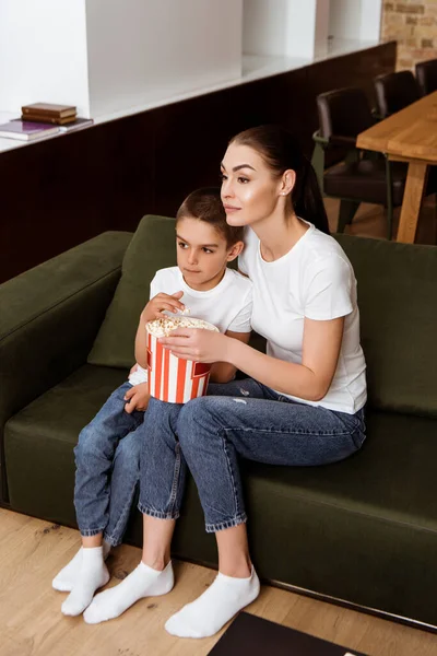 Mère et enfant manger du pop-corn tout en regardant un film sur le canapé à la maison — Photo de stock