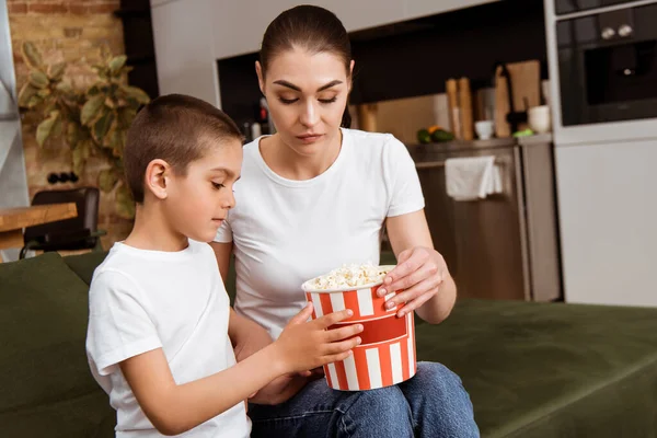 Mother and kid holding bucket with popcorn on couch at home — Stock Photo