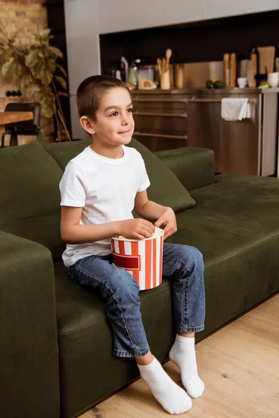 Kid segurando balde de pipocas enquanto assiste filme no sofá — Fotografia de Stock