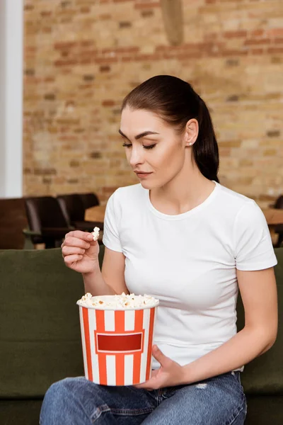 Donna attraente che tiene popcorn sul divano a casa — Foto stock