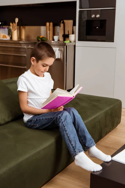 Selective focus of child reading book on couch at home — Stock Photo