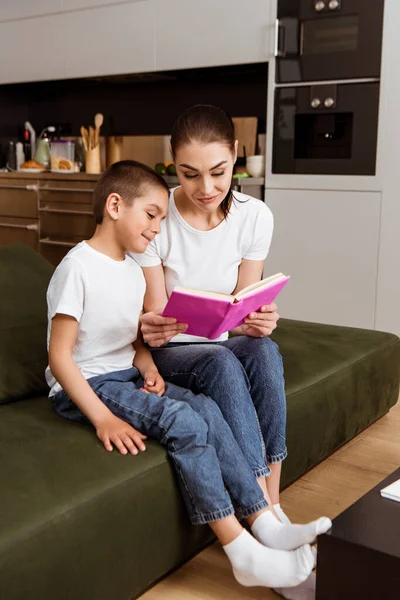 Selective focus of mother and smiling son reading book on sofa — Stock Photo
