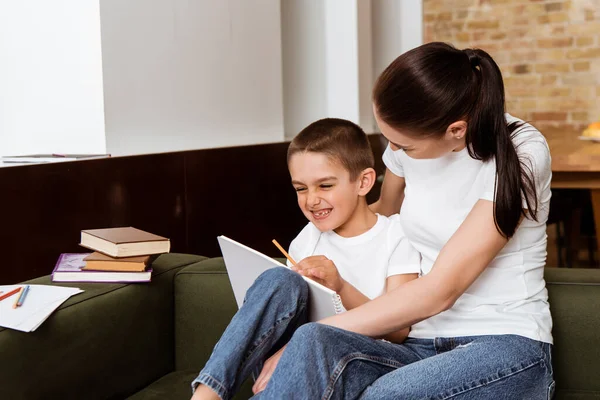 Madre seduta vicino al figlio allegro con matite e sketchbook sul divano a casa — Foto stock