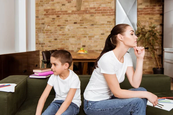 Trauriger Junge sitzt neben Mutter, Bücher und Buntstifte mit Papier auf Couch — Stockfoto