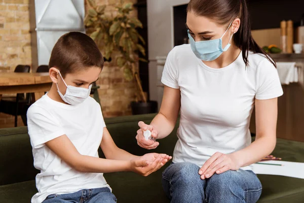 Мати і син в медичних масках використовують дезінфікуючий засіб для рук вдома — стокове фото