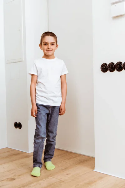 Улыбающийся ребенок смотрит в камеру, стоя дома в коридоре — стоковое фото