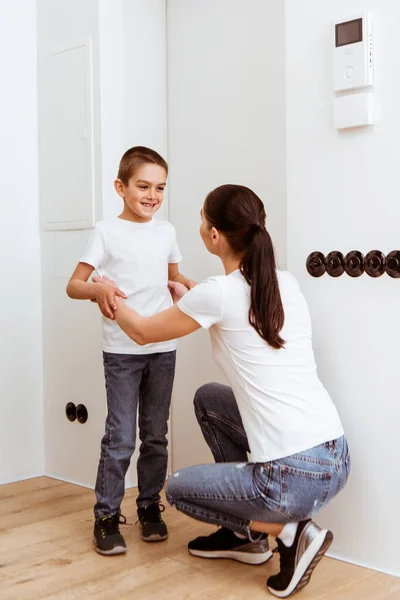 Mutter umarmt lächelnden Sohn vor Tür im Hausflur — Stockfoto