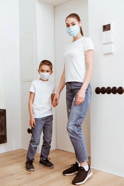 Мать и сын в медицинских масках держатся за руки в коридоре — стоковое фото