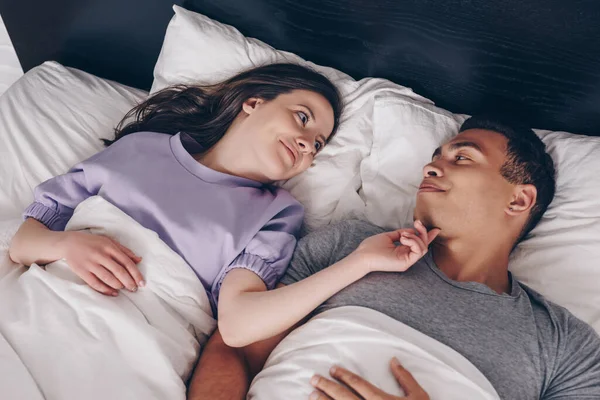 Overhead view of cheerful woman touching mixed race boyfriend in bed — Stock Photo