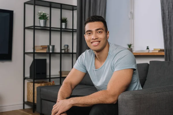 Glücklich gemischte Rasse Mann sitzt auf Sofa im Wohnzimmer — Stockfoto